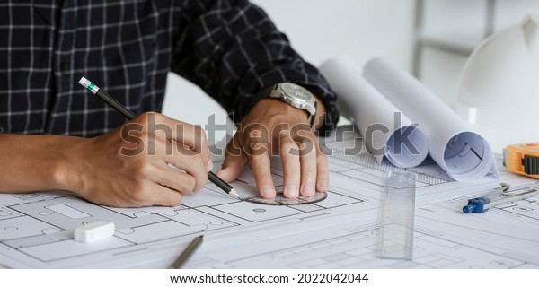 Close up of engineer drawing on blueprint\
architectural project at a desk in the office. inspection workplace\
for architectural plan, sketching a construction project.\
Construction concept