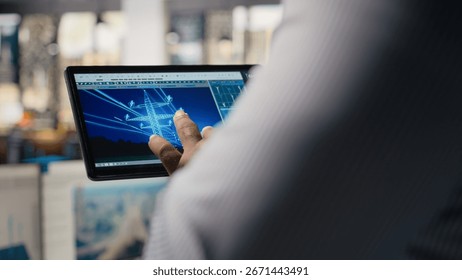 Close up of engineer using tablet to design power line towers in office. RD department specialist uses CAD software on device to optimize transmission tower systems, camera A