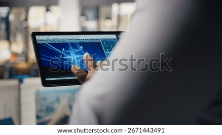 Close up of engineer using tablet to design power line towers in office. RD department specialist uses CAD software on device to optimize transmission tower systems, camera A
