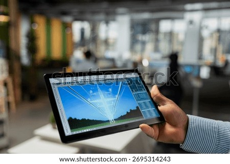 Close up of engineer using tablet to refine transmission tower systems, improving renewable energy integration. RD expert uses touchscreen device in office to design eco power lines infrastructure