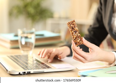 Close up of entrepreneur woman hands holding cereal snack bar working on laptop at home office
