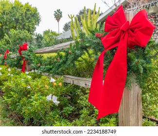 Close up of an evergreen Christmas wreath with a red ribbon hangs on a fence post. - Powered by Shutterstock