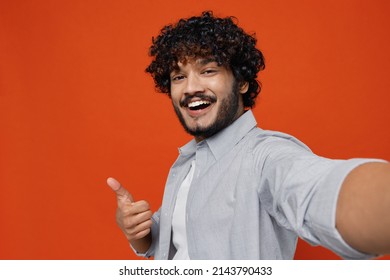 Close up excited smiling fun jubilant exultant young bearded Indian man 20s years old wears blue shirt showing thumb up like gesture looking camera isolated on plain orange background studio portrait