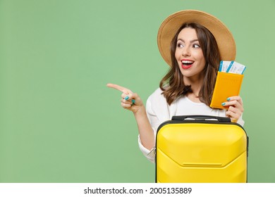 Close up excited tourist woman in casual clothes hat hold passport ticket suitcase point finger aside workspace isolated on green background Passenger travel abroad weekend getaway Air flight concept