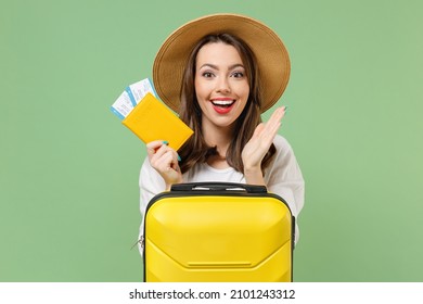 Close up excited tourist woman in casual clothes hat hold passport tickets yellow suitcase spread hands isolated on green background Passenger travel abroad weekend getaway Air flight journey concept.