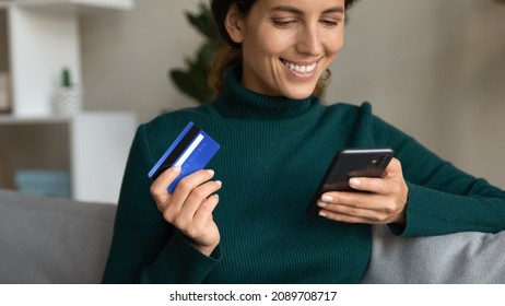 Close Up Of Excited Young Hispanic Woman Relax At Home Shop Online On Cellphone With Credit Debit Card. Smiling Latino Female Buyer Make Purchase Pay Or Buy On Internet On Smartphone With Banking App.