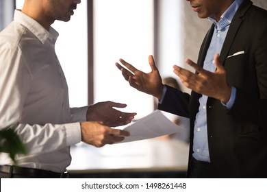 Close up executive manager dissatisfied by African American employee work results, holding financial report with stats, colleagues arguing, discussing business failure, partners disputing at work