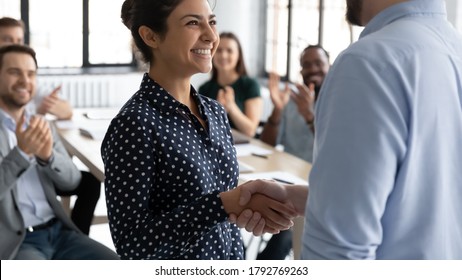 Close up executive shaking smiling Indian businesswoman hand at meeting, diverse colleagues applauding, team leader congratulating successful employee with job promotion, thanking for good work