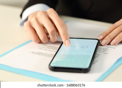 Close up of executive woman hands signs contract on smart phone with finger sitting on a desk
