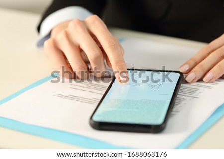 Close up of executive woman hands signs contract on smart phone with finger sitting on a desk