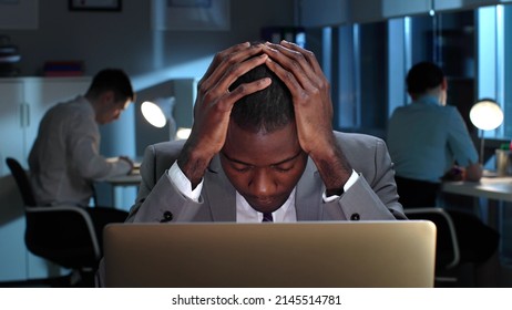 Close up of exhausted African-American lawyer working late on laptop in business center. Tired startup entrepreneur sitting at desk in dark office