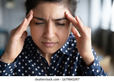 Close up exhausted Indian girl touching forehead, unhappy upset girl suffering from strong headache or migraine, overworked tired young female feeling pain in head, health problem concept - Powered by Shutterstock