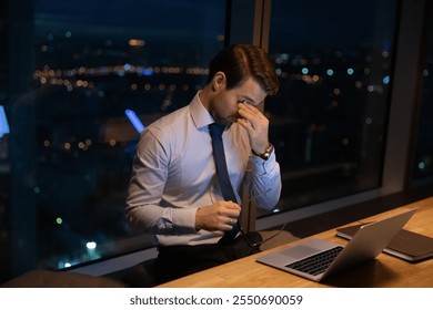 Close up exhausted overworked businessman taking off glasses, massaging nose bridge, suffering from eye strain, dry eyes syndrome, working at night, sitting at desk with laptop, deadline concept - Powered by Shutterstock