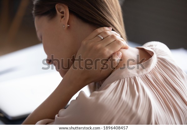 Close up exhausted woman touching massaging tensed\
neck muscles, feeling unwell after long hours sedentary work,\
uncomfortable chair, incorrect posture, young female suffering from\
pain, ache