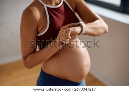 Close up of expecting mother using app on smart watch while exercising at home. 
