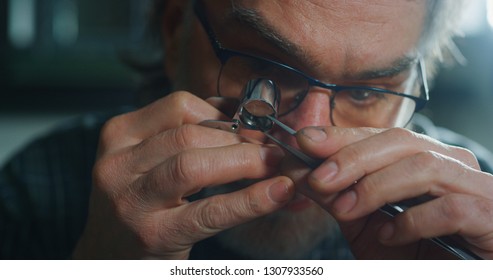 Close up of experienced goldsmith controlling a quality of emerald, selected for making jewels in workshop.Concept of jewelry,luxury,goldsmith, diamonds, brilliance.