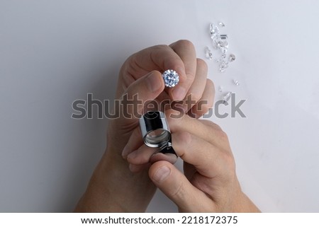 Close up of an expert's hand evaluating the quality of a round cut diamond trough a magnifying glass top view.
