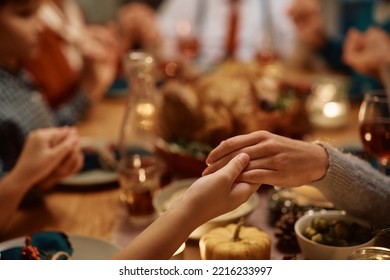 Close up of extended family saying grace during Thanksgiving dinner at dining table.