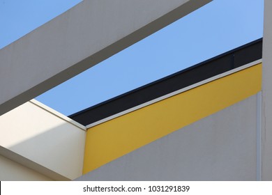 Close up exterior view from below of the top of a modern painted building. Geometric forms colored in white, gray, black and yellow. Opening with the blue sky in background. Many polygonal shapes.  - Powered by Shutterstock