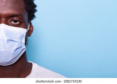 Close Up Of Eye Of African American Person With Face Mask While Looking At Camera. Black Face With Protection Against Coronavirus Epidemic For Healthcare, Standing Over Blue Background