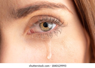 Close up of the eye cheek of a young woman with a tear running down her cheek.  