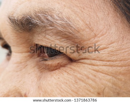 Close up of eye and grey eyebrown of an old woman showing crow's feet and wrinkles from aging 