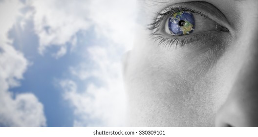 Close up of eye looking up against bright blue sky with clouds