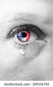  Close up eye of young man crying sad in tears with french flag reflection on his iris, black and white isolated color edition