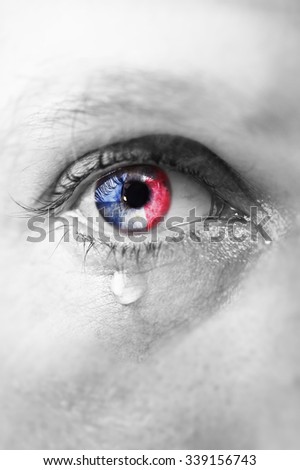  Close up eye of young man crying sad in tears with french flag reflection on his iris, black and white isolated color edition