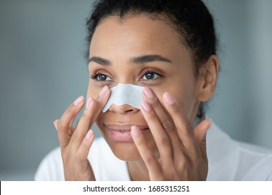 Close up face of 30s African ethnicity woman apply white cleansing nose strip for deep purifying and blackheads removal. Modern cosmetology treatment for ideal healthy beautiful skin, skincare concept