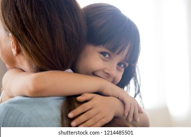 Close Up Face Adorable Preschool Little Mixed Race Daughter Looking At Camera Smiling Embrace Her Loving Young Mother, Mom Rear View. Happy Wellbeing Family Or New Mum For Adopted Child Concept