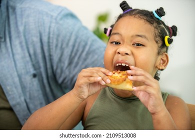 Close Up Face Of African Child Girl Kid Biting And Eating Tasty Pizza With Happiness. Happy Family Parents With Little Cute Daughter Enjoy Having Dinner Eating And Sharing A Meal Together At Home