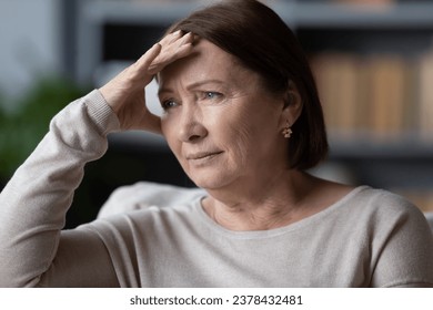 Close up face of attractive 60s woman seated on couch touch forehead with hands thinking about life troubles, personal or health problems feels disappointed or concerned, middle-aged crisis concept - Powered by Shutterstock