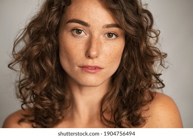 Close Up Face Of Beautiful Woman With Healthy Natural Skin Looking At Camera. Portrait Of Young Woman With Nude Shoulder. Portrait Of Sensual Girl With Freckles Isolated Against Grey Wall Background.