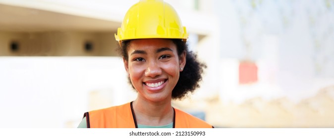 Close Up Face Black Woman. Portrait Femal African American Engineer Worker Wearing Yellow Hard Hat Helmet Working On Construction Site.