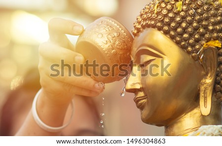 Close up Face of Buddha statue with Hand of sprinkle water onto a Buddha image. Buddhism ceremony of religion, Believe of Buddhist .  Merit and worship. Songkran the most famous festival of Thailand.