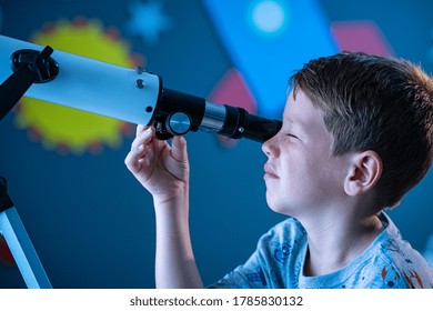 Close Up Face Of Curious Kid Child Using Telescope To Explore Moon Surface. Little Boy Stargazing At Night With A Telescope To See Galaxy From His Room Decorated Bedroom With Rocket In Background.