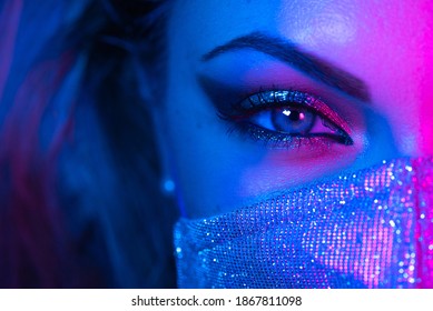 Close Up Of Face In Glitter Protective Mask, Amazing Make-up. Eye Under Neon Light. Female With Shining Shadows And False Lashes. Nightlife, Night Club, Pandemic, Covid-19 Concept.