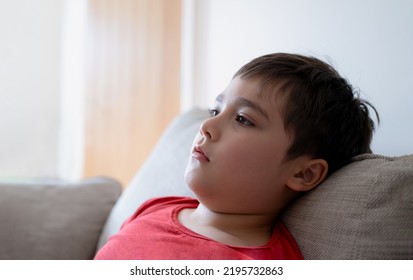 Close Up Face Kid With Curious Face, Side View Portrait Child Sitting On Couch Looking Out Deep In Thought. Cute Young Boy Sitting On Sofa Wathcing TV Or Relaxing At Home On Weekend.