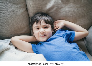 Close up face of kid looking at camera with smiling, A happy boy lying on sofa relaxing on weekend, Comfortable Child laying down on couch and looking out, Positive children concept