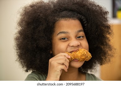  Close Up Face Of Little African Girl Biting And Eating Tasty Deep Fried Chicken With Happiness. Happy Family Parents With Two Daughter Enjoy Having Dinner Eating And Sharing A Meal Together At Home.