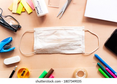 Close Up Of Face Mask On Wood Desk In Classroom With Mobile Phone And Block Notes And Education Equipment. Concept Of Prevention Of Covid At School