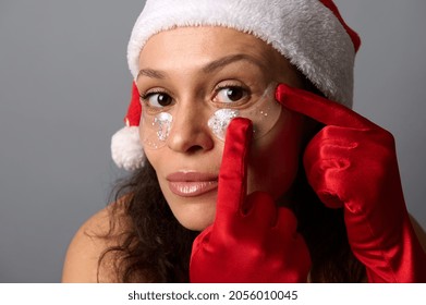 Close Up Face Portrait Of Pretty Brunette Woman In Santa Hat Wearing Eye Patches Looking Closely At Camera, Isolated On Gray Background. Skin Care Concept For Christmas Ad Of Cosmetology Beauty Salons