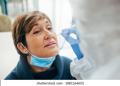 Close up of the face of senior female patient being tested for Covid-19 with a nasal swab, by a health Professional protected with gloves and PPE suit. Rapid Antigen Test during Coronavirus Pandemic.