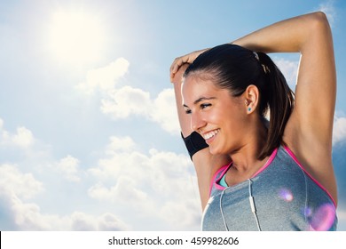 Close up face shot of attractive  young runner getting ready for morning run.Woman with charming smile stretching arms and neck against sunny sky.