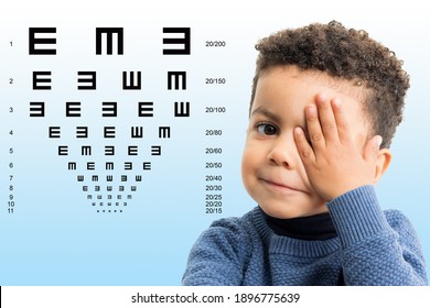 Nahaufnahme eines kleinen Afro-Amerikaners, der das Sehvermögen testet. Kind, das sich mit der Hand auf dem Auge schließt. Sehdiagramm mit Blockbuchstaben im Hintergrund.