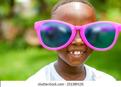 Close up face shot portrait of cute African boy wearing huge over sized sun glasses outdoors.