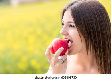 Close up face shot of Young woman biting red apple outdoors.