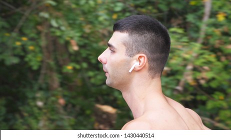 Close Up Face Of Young Strong Sportsman Running Along Trail Near Forest. Athletic Man With Wireless Headphones Jogging At Early Autumn. Handsome Guy Running Outdoor. Healthy Active Lifestyle. Slow Mo