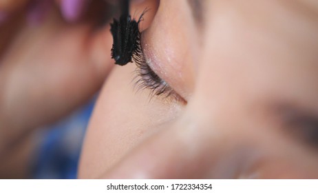 Close up face of young woman applying cosmetic on eyelashes. Pretty girl with wide opening eyes doing makeup with mascara. Attractive model in beauty salon. Concept of fashion and style. Isolated shot